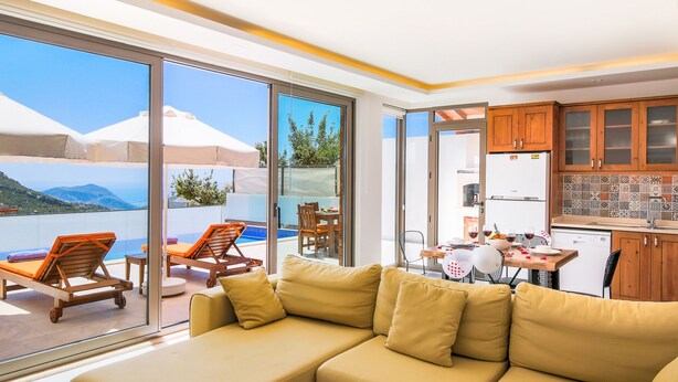 A modern living room with a beige sofa, a dining area with a table and chairs, and a kitchen with wooden cabinets and a refrigerator.