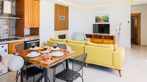 A compact living space with a dining area, yellow sofa, TV, and kitchen.