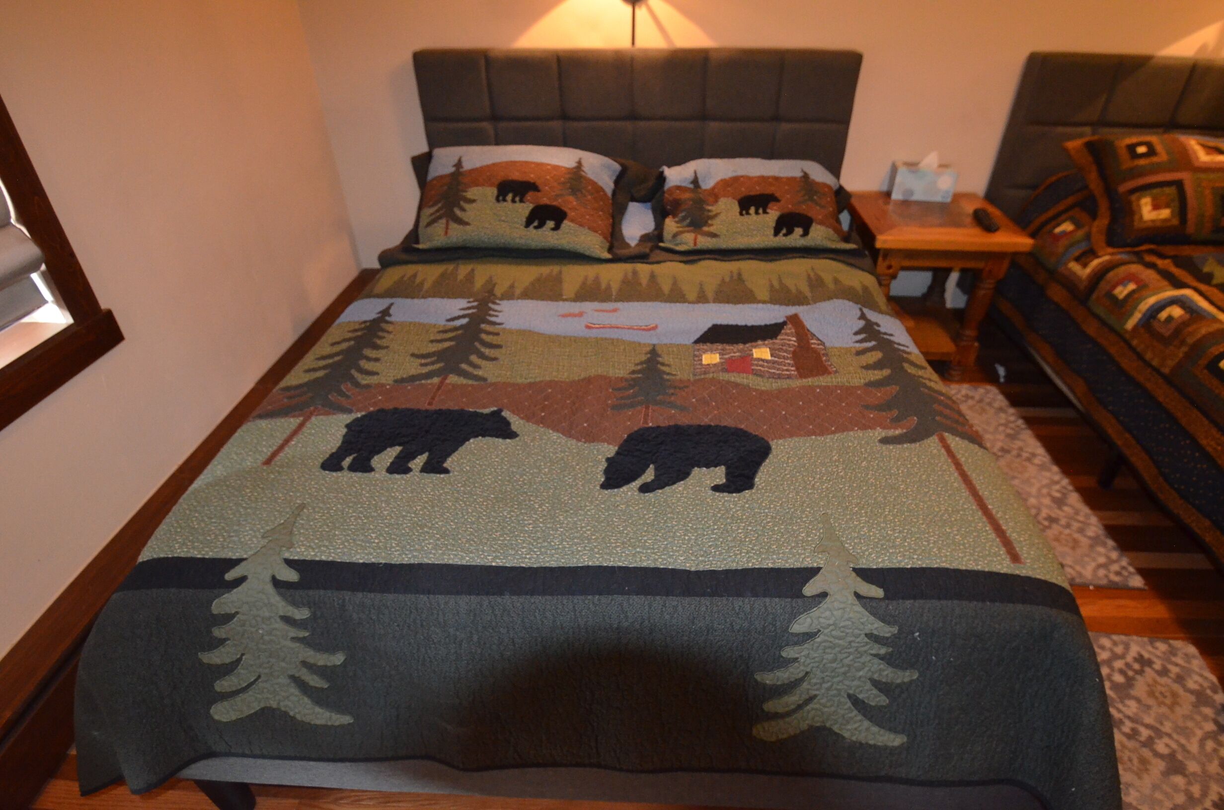 A bed with a forest-themed bedspread, a headboard, and a nightstand with a lamp.