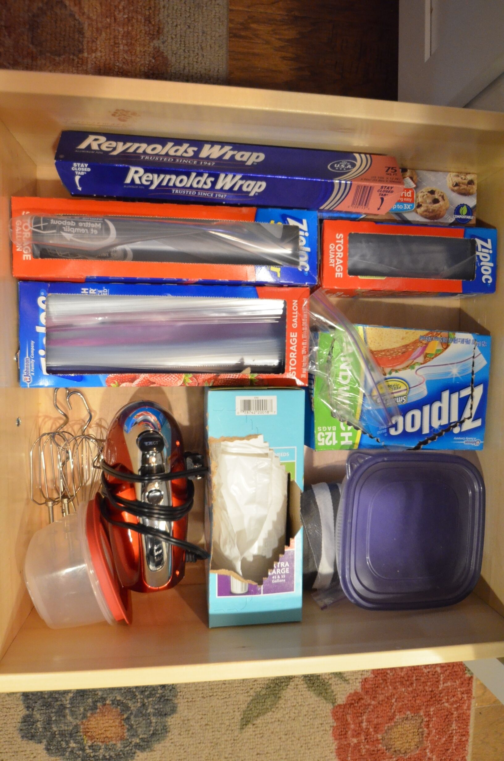 Uma gaveta com diversos itens de organização, incluindo sacos Ziploc, um aspirador de pó e caixas organizadoras.