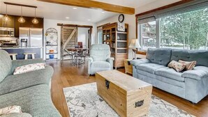 A spacious living room with a grey sofa, a wooden coffee table, and a light blue armchair. A staircase leads to a dining area with a table and chairs. - Mountain Comfortable Colorado Lodging in Frisco CO - Sleeps 8 - 1 block off Main (Frisco)