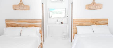 A hotel room with two beds, a window, a sink, and a hanging light fixture.