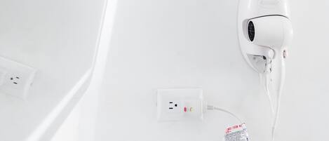 A white hairdryer plugged into a wall socket with a power adapter.