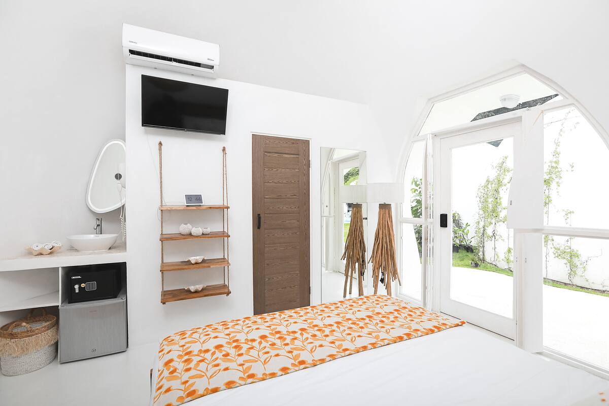 Quarto com cama, televisão, guarda-roupa, pia e janela com vista para o verde.