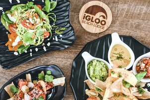 Una mesa de madera con tres platos negros de comida, incluyendo tacos, guacamole y una ensalada.