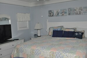 Een slaapkamer met een bed, een televisie, een lamp en kunst aan de muur.