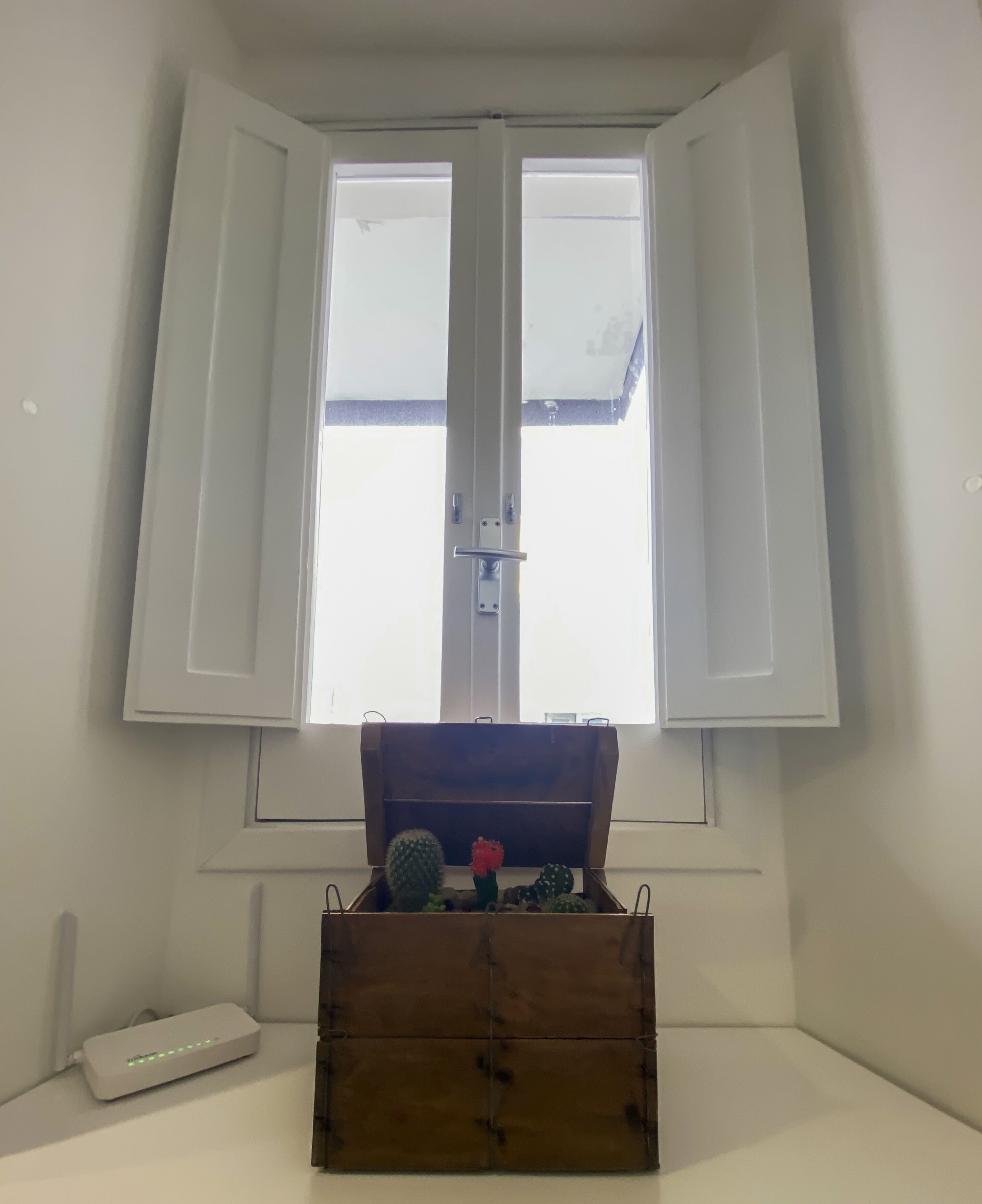 A room with a window, a wooden chest, and a white device on the floor.