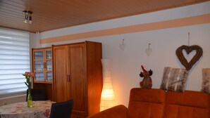 Un salon chaleureux avec un meuble en bois, une table recouverte d’une nappe à motifs floraux et un canapé.