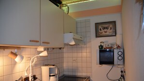 Une cuisine avec des meubles blancs, une machine à café, un four à micro-ondes et une petite étagère ornée d’objets décoratifs.