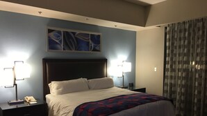 A hotel room with a large bed, two bedside tables, a nightstand, a wall-mounted artwork, and a window with curtains. - Beautiful Marriott Timeshare Unit located adjacent to JW Marriott (Palm Desert)