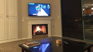 A living room with a fireplace, a television mounted above it, and a coffee table with a book and remote control. - Beautiful Marriott Timeshare Unit located adjacent to JW Marriott (Palm Desert)