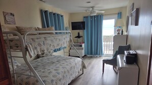 A room with bunk beds, a desk, a chair, a television, and a balcony with curtains. - Oceanfront 3 Bedroom 3 Full Bath Townhome With Panoramic Views Of The Ocean  (Seaside Park)