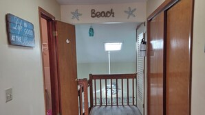 A hallway with a wooden floor, a sofa with patterned cushions, a ceiling light, and a sign that reads 'Beach.' - Oceanfront 3 Bedroom 3 Full Bath Townhome With Panoramic Views Of The Ocean  (Seaside Park)