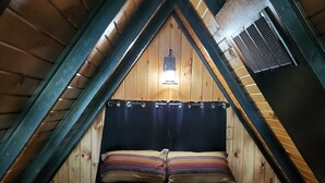 Une chambre mansardée chaleureuse avec un plafond en pente en bois, un lit avec une literie à rayures, un rideau noir et un luminaire fixé au mur.
