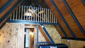 Une pièce de style « loft », avec un intérieur en bois, un plafond en pente et un balcon doté d’une balustrade.