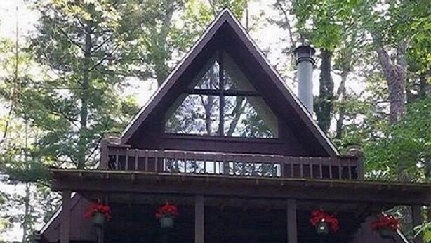 Une cabane en bois à deux étages, dotée d’un balcon, d’un porche à l’avant et d’un escalier menant à l’entrée.