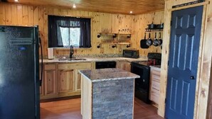 Une cuisine avec des meubles en bois, un îlot central doté d’un comptoir en granit et un réfrigérateur noir.