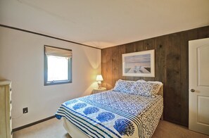 A bedroom with a bed, a nightstand, a lamp, a framed picture, and a window.