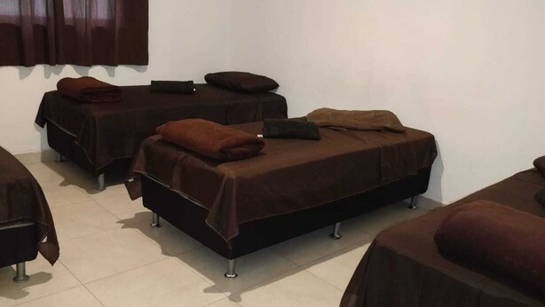 A room with four beds, each covered with a brown blanket and pillows. - Ed. HSS (Ouro Preto)