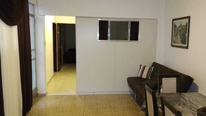 A living room with a sofa, a small table, a picture on the wall, and a window. - Ed. HSS (Ouro Preto)
