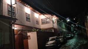 A narrow street with buildings on both sides, a gated entrance, and parked cars. - Ed. HSS (Ouro Preto)