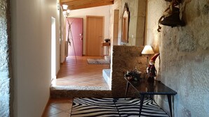Un corridoio con un tappeto a motivi zebrati, travi in legno, pareti in pietra, una porta in legno, un tavolino con una lampada e uno specchio appeso al muro.