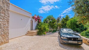 Un bâtiment en pierre avec une voiture garée devant, un ciel dégagé et une végétation luxuriante.