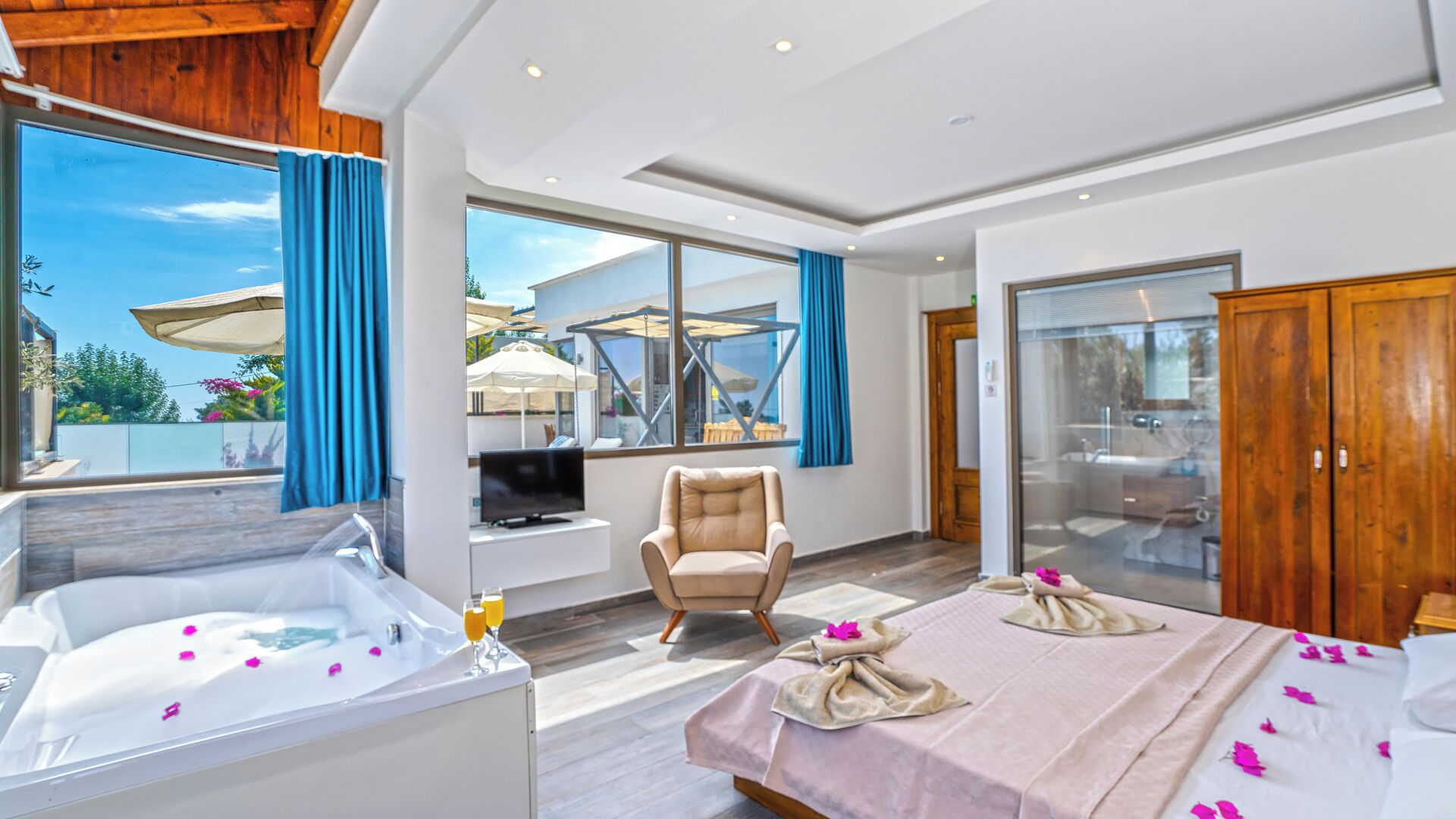 A modern hotel room with a large bed, a sitting area with a chair, a TV, and a view of the outdoors.