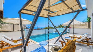 A poolside area with a swing chair, lounge chairs, and umbrellas.