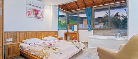 Une chambre à coucher avec un lit en bois, un bureau, une chaise, une baignoire et une grande fenêtre donnant sur un paysage verdoyant.