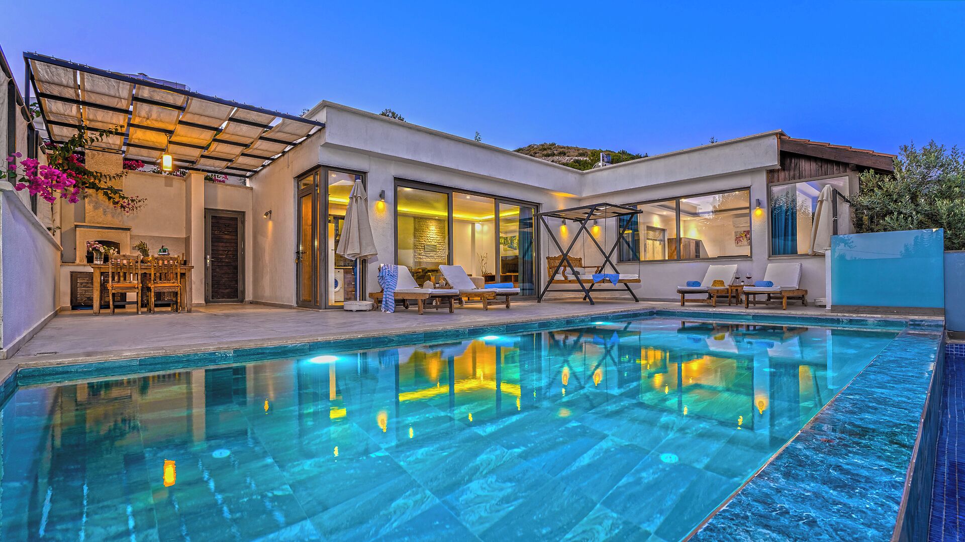 A modern poolside area with a clear pool, sun loungers, and a covered seating area.
