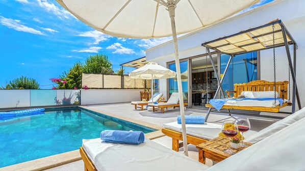 Un área junto a la piscina con una hamaca, sillas de descanso y sombrillas.