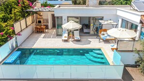 Un área de piscina moderna al aire libre con un jacuzzi integrado, sillas de descanso y sombrillas.