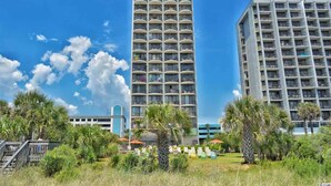 A tall hotel with multiple balconies, surrounded by palm trees and a clear sky. - Gorgeous Oceanfront Condo With Direct Ocean View (Myrtle Beach)
