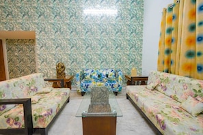 A living room with floral-patterned sofas, a glass coffee table, and a decorative statue. - Homestay worth exploring (Raipur)