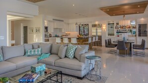 A modern living room with a sofa, coffee table, and a dining area with chairs. - Thanksgiving Promo!!  Your Exclusive Cabo Beachfront Escape (Cabo San Lucas)