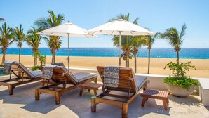 A beachside lounge area with wooden lounge chairs, white umbrellas, and a view of the ocean. - Thanksgiving Promo!!  Your Exclusive Cabo Beachfront Escape (Cabo San Lucas)