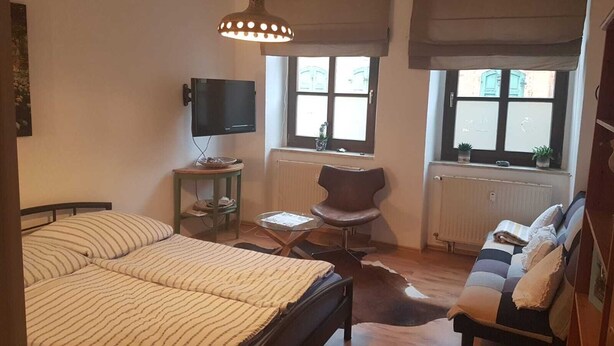 Une chambre à coucher avec un lit, une chaise, un téléviseur et une fenêtre avec des stores.