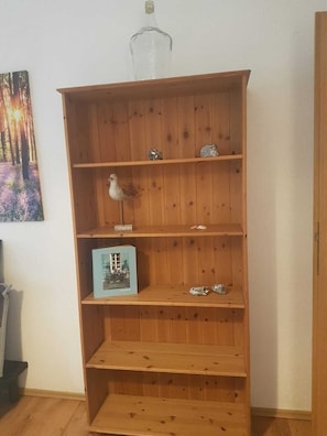 Une bibliothèque en bois à trois étagères, avec une bouteille en verre sur l’étagère supérieure et une figurine d’oiseau sur l’étagère du milieu.