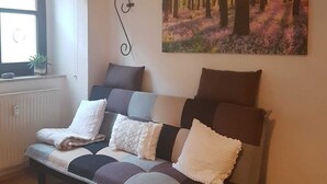 Un salon chaleureux avec un canapé, un tableau représentant une forêt et une petite table sur laquelle est posée une bougie.