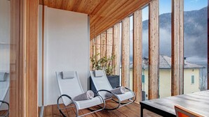A wooden deck with two lounge chairs and a table, overlooking a mountainous landscape.