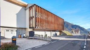 A modern building with a unique facade, a paved road, and a mountainous backdrop.