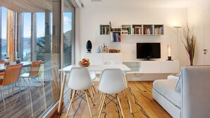 A modern living room with a dining area, a flat-screen TV, and a bookshelf.