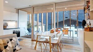 A modern kitchen with white cabinets, a dining area with a white table and chairs, and large windows offering a view of a house and trees.