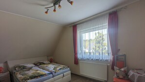 Un dormitorio con cama, una silla, una mesa y un ventanal con cortinas.