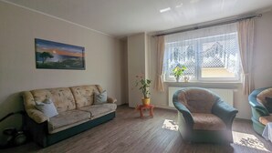 Una sala de estar con un sofá, una silla, un cuadro y una ventana con cortinas.
