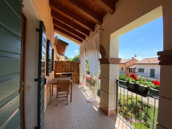 A balcony with a wooden table and chairs, a tiled floor, and a view of the neighborhood.