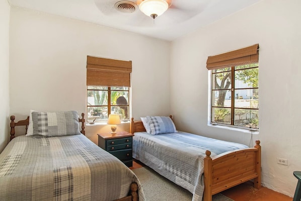 A bedroom with two single beds, a nightstand with a lamp, and windows with blinds. - Casa del Rio | Pet-Friendly River Stay with Views (Bandera)