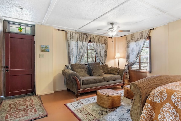 A room with a wooden door, a sofa with cushions, a patterned rug, and a ceiling fan. - Casa del Rio | Pet-Friendly River Stay with Views (Bandera)