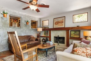 A living room with a fireplace, a ceiling fan, and a variety of decorative items. - Casa del Rio | Pet-Friendly River Stay with Views (Bandera)